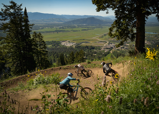 Three mountain bikers on trail at Jackson Hole Mountain Resort in the summer with views of Jackson below