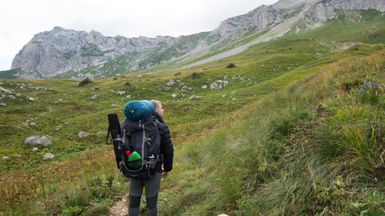 A man with a large hiking backpack treks up a rugged mountain