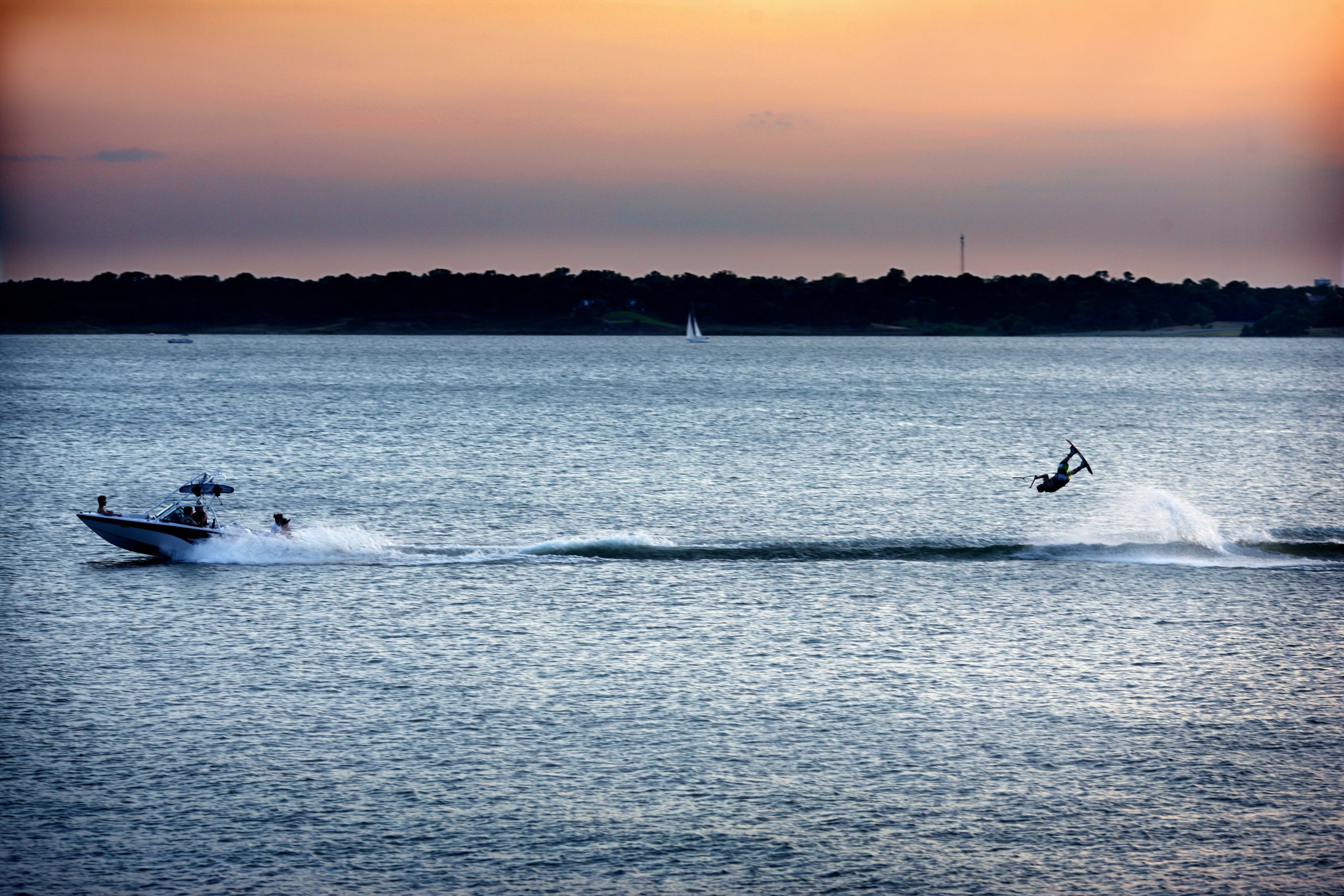 A boat pulls a person on a wakeboard on a Lake Grapevine at sunset, with a shoreline in the distance. Grapevine, Texas.