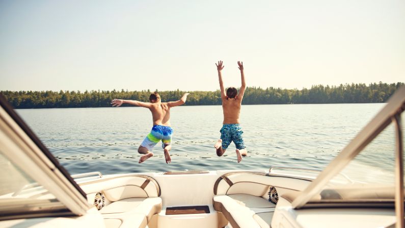 Two boys jumping off a boat into some calm water