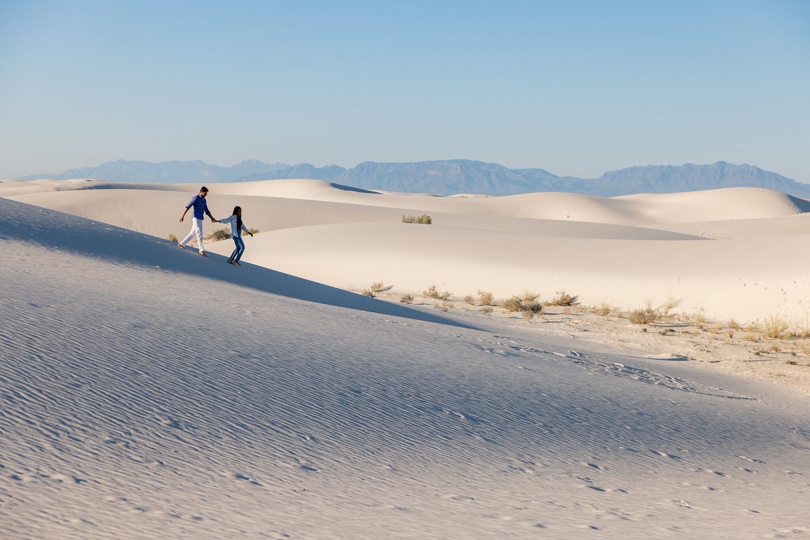 A couple walks hand in hand across the white gypsum dunes of White Sands National Park.