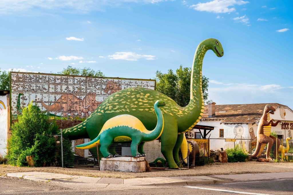 Large green dinosaur sculptures line the sidewalk of a Route 66 roadside rock shop in Holbrook, Arizona.