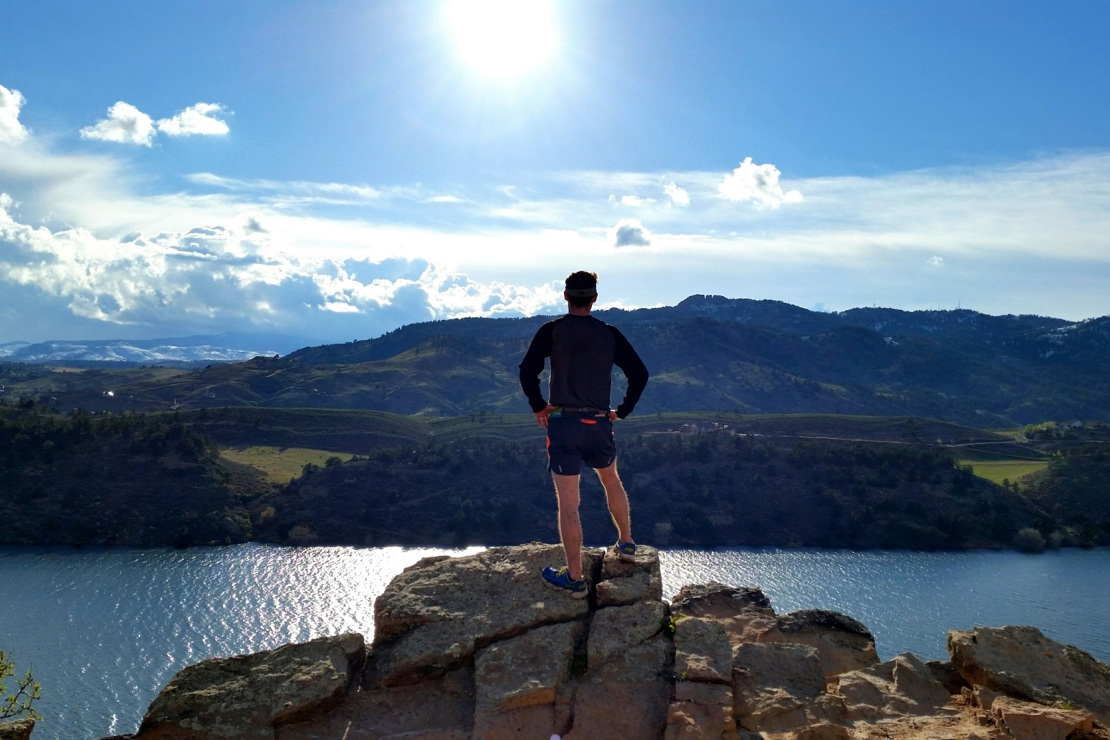 Man standing on a rock overlooking a lake with mountains in the background.