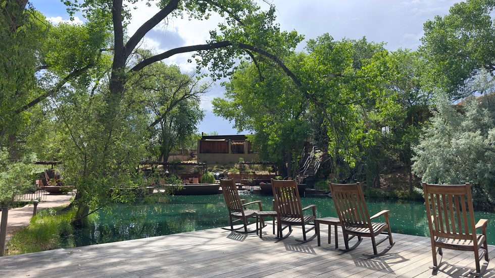 Covered outdoor patio dining area at El Nido with white-clothed tables, string lights, patio heaters, and diners seated beneath a wooden pergola roof. Santa Fe County.