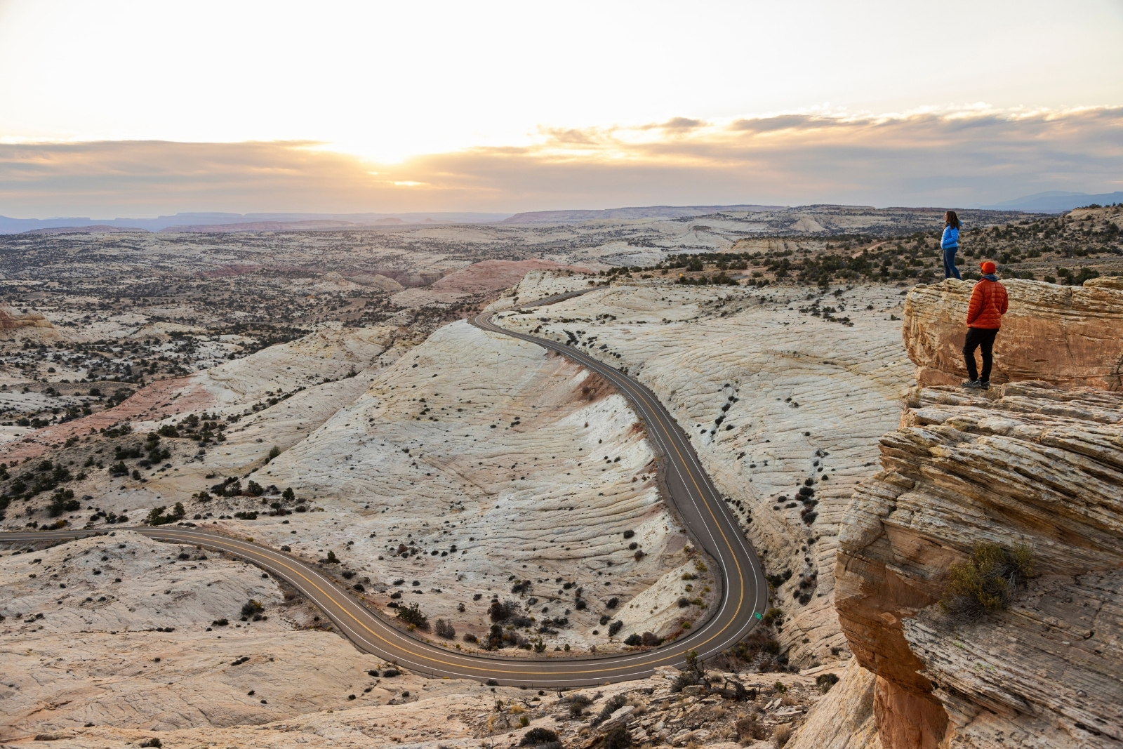 Two people standing on a cliff overlooking a road cutting through a white stone desert